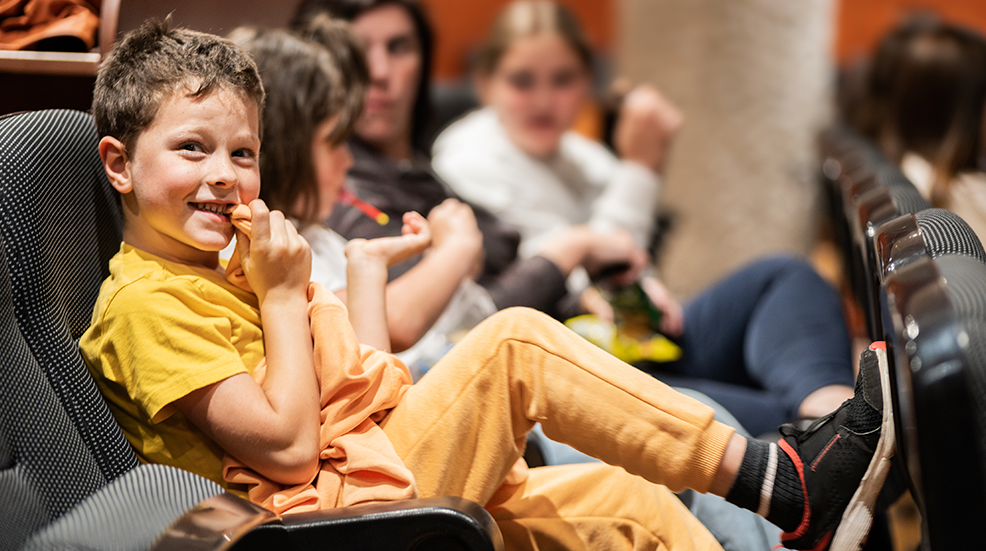 A young boy looking excited sat in a cinema seat ready for the film to start